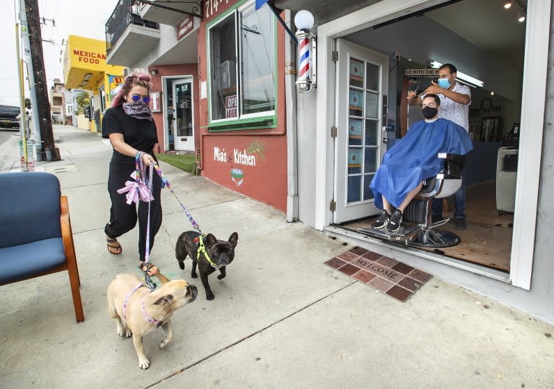 MANHATTEN BEACH, CA -JULY 29, 2020: Faro Tabaja, owner of Waves Barbershop & Boutique on Rosecrans Ave. in Manhattan Beach, gives a haircut to Gene Geiser of Manhattan Beach. Tabaja moved the barber's chair into the entry way to create a safer environment to cut hair due to the coronavirus outbreak. (Mel Melcon / Los Angeles Times)