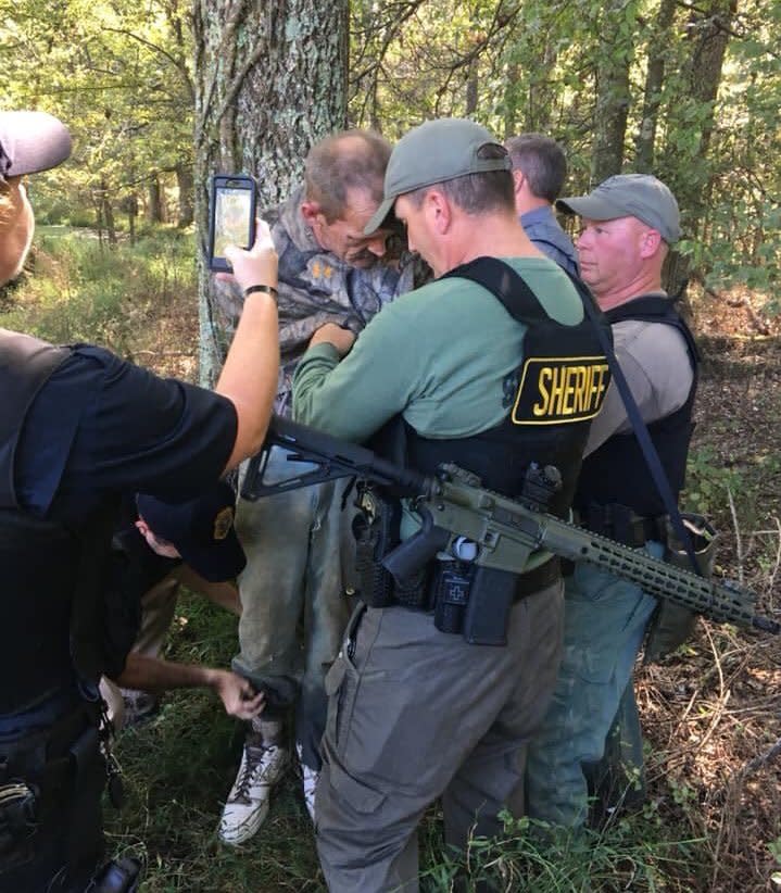 This photo provided by The Tennessee Bureau of Investigation shows law enforcement agents holding Kirby Wallace in custody on Friday, Oct. 5, 2018 in Tennessee. Wallace is wanted on multiple charges after being accused of attacking a couple and setting their house on fire, killing the wife and seriously injuring the husband. He's also accused of fatally shooting a man Monday and stealing his truck. (The Tennessee Bureau of Investigation via AP)