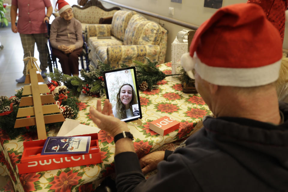 Roberto Capellini, is flanked by carer Michela Valle, right, and director Maria Giulia Madaschi, as he talks on video call with Carolina Giannesi, a donor unrelated to her, who bought and sent her a Christmas present through an organization dubbed "Santa's Grandchildren", at the Martino Zanchi nursing home in Alzano Lombardo, one of the area that most suffered the first wave of COVID-19, in northern Italy, Saturday, Dec. 19, 2020. (AP Photo/Luca Bruno)