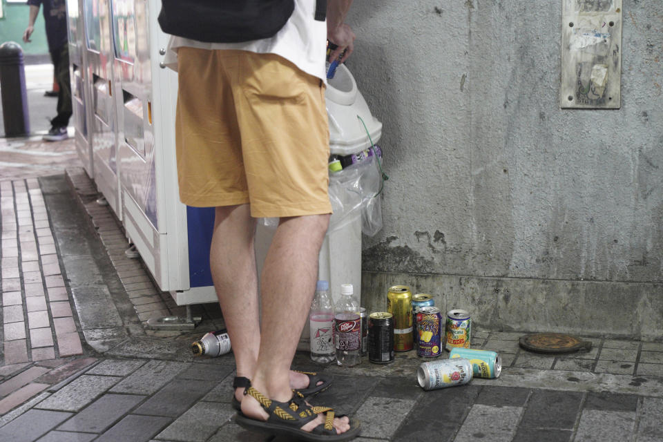 A young man throws a beer can to already full garbage box in Tokyo’s Shinjuku district Monday, July 19, 2021. The latest state of emergency has asked restaurants and bars to close by 8 p.m., if not entirely. This has pushed people to drink outside, although many bars remain open and bustling with customers who are defying the rules and expressing frustration and indifference. (AP Photo/Kantaro Komiya)
