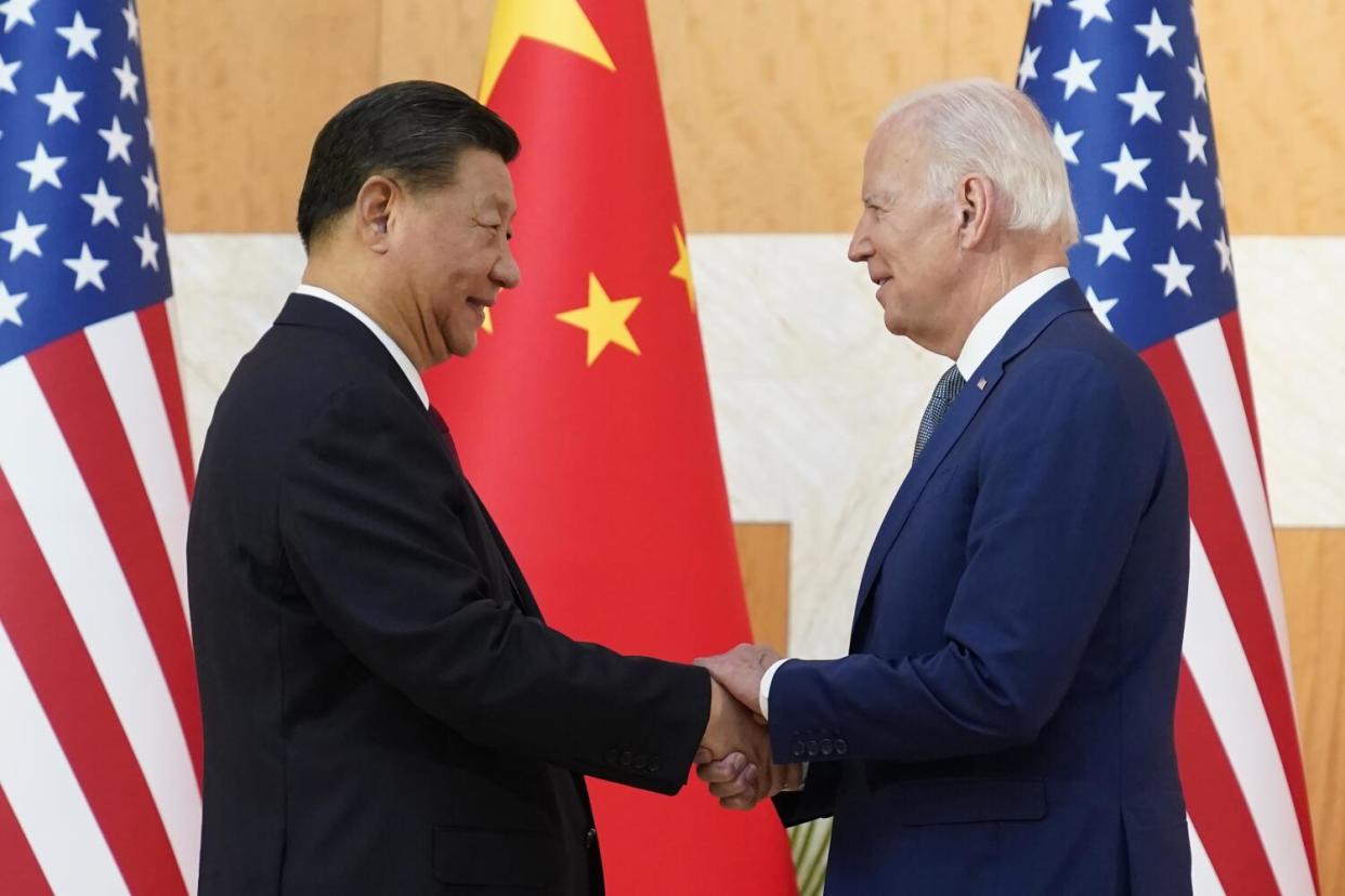 Two men shake hands in front of flags.