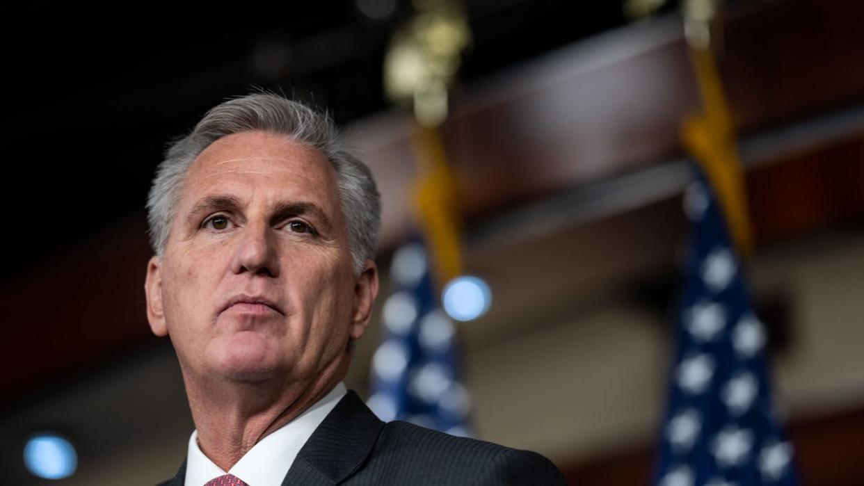 kevin mccarthy looks past the camera with a neutral expression, he wears a dark suit jacket, white shirt and red patterned tie