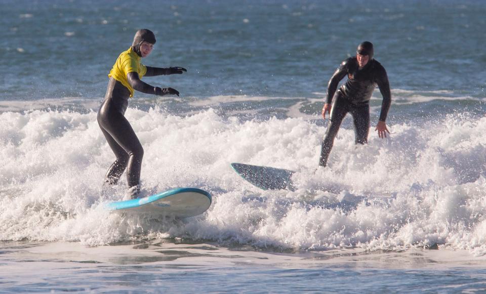 Makenzie Elliott, left, gets up on a surfboard for the first time during a lesson with Dan Hasselschwert, owner of Ossies Surf Shop in Newport on Nov. 19.