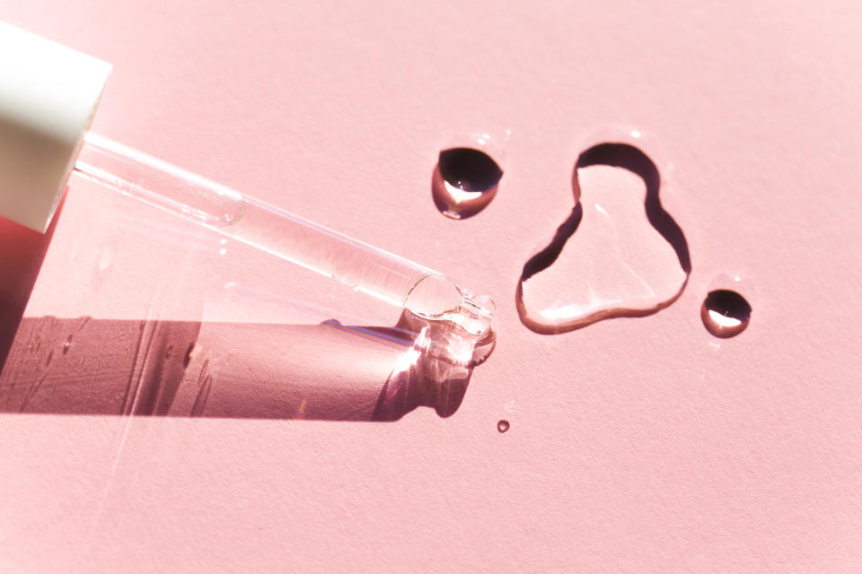 From above closeup transparent drops of clean lotion and glass pipette placed on pink background