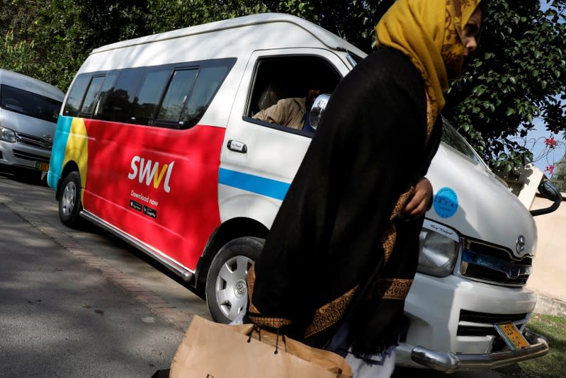 A woman walks past a vehicle with a logo of the Egyptian transport technology start-up Swvl, parked along a road in Islamabad
