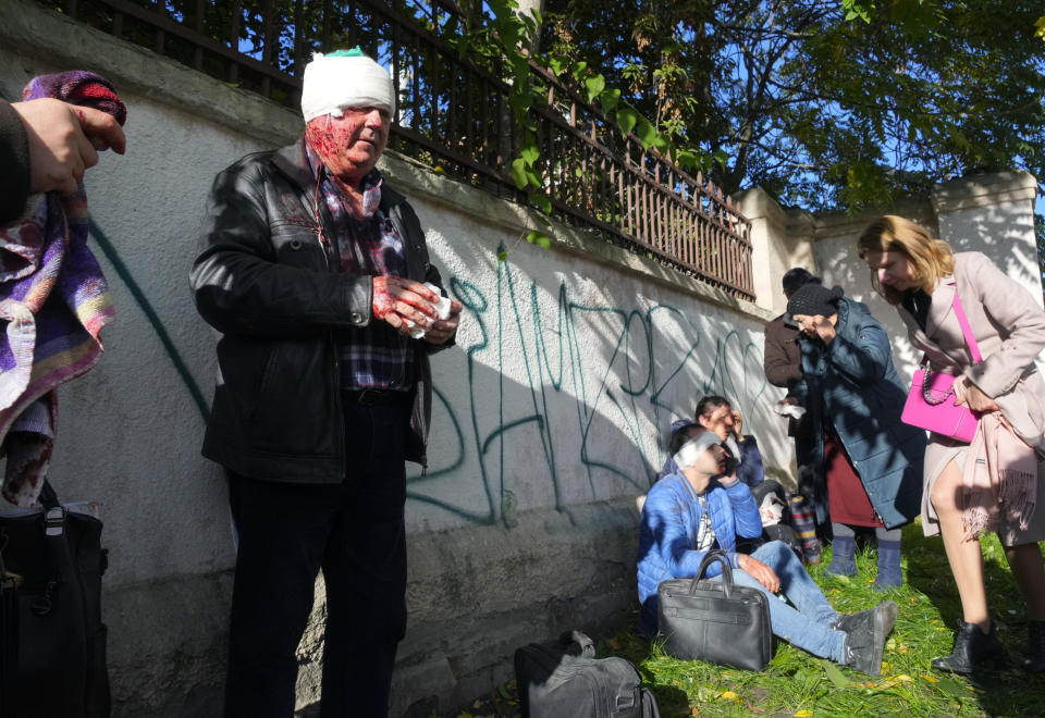 People receive medical treatment at the scene of Russian shelling, in Kyiv, Ukraine, Monday, Oct. 10, 2022. Multiple explosions rocked Kyiv early Monday following months of relative calm in the Ukrainian capital. Kyiv Mayor Vitali Klitschko reported explosions in the city's Shevchenko district, a large area in the center of Kyiv that includes the historic old town as well as several government offices. (AP Photo/Efrem Lukatsky)