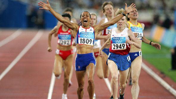 Dame Kelly Holmes holds both arms aloft as she crosses the finish line ahead of competitors during the final of the women's 1500m at the Olympic Stadium.
