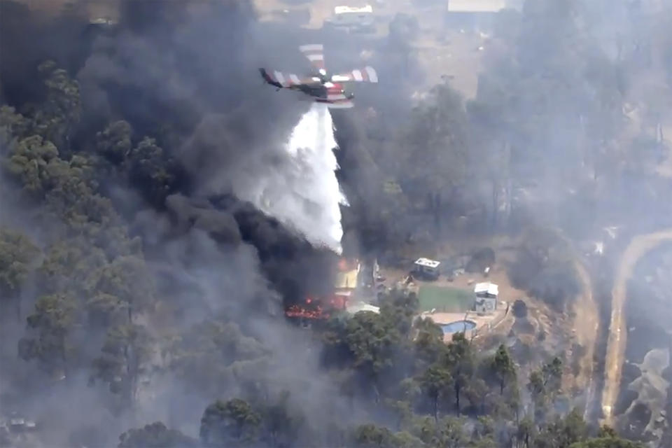 This image made from video shows helicopter dropping water on flames, thick black smoke billowing outside Perth, Australia, Thursday, Dec. 21, 2023. A wildfire burning out of control on the outskirts of the Australian west coast city of Perth on Thursday appeared to have destroyed or damaged a number of homes. (Australian Broadcasting Corp/Channel 7/Channel 9 via AP)