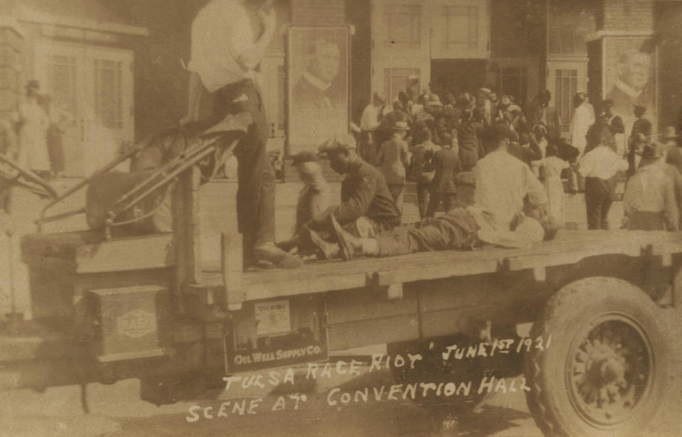 This postcard provided by the Department of Special Collections, McFarlin Library, The University of Tulsa shows a truck parked in front of the Convention Hall, with a man whose condition is unknown, lying on the bed of the truck, and two others sit to either side. A man in civilian attire stands guard over them during the Tulsa Race Massacre June 1, 1921, in Tulsa, Okla. (Department of Special Collections, McFarlin Library, The University of Tulsa via AP)