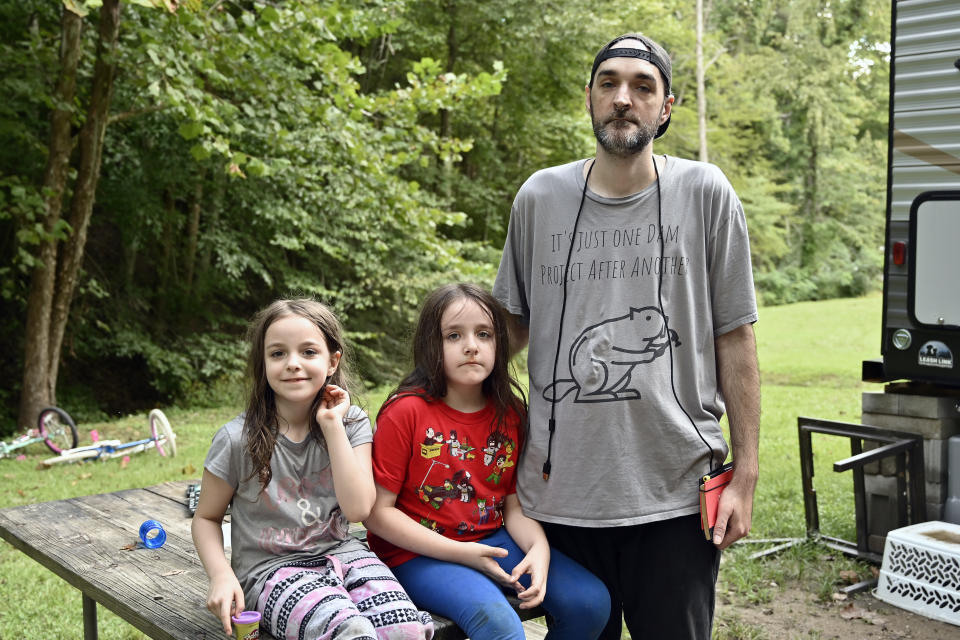 From left, Kerrigan Stephens, Loki Stephens and their father David Stephens outside their travel trailer at Jenny Wiley State Park in Prestonsburg, Ky., Tuesday, Sept. 6, 2022. When floodwaters rook everything they had in late July, they stayed in a motel, but now are temporarily in a trailer. (AP Photo/Timothy D. Easley)