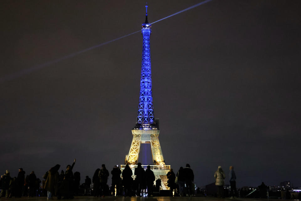 Bystanders watch the Eiffel Tower lit in the colours of the Ukrainian flag in a show of support to Ukraine, one year after Russia launched a military invasion on the country, in Paris on February 23, 2023.