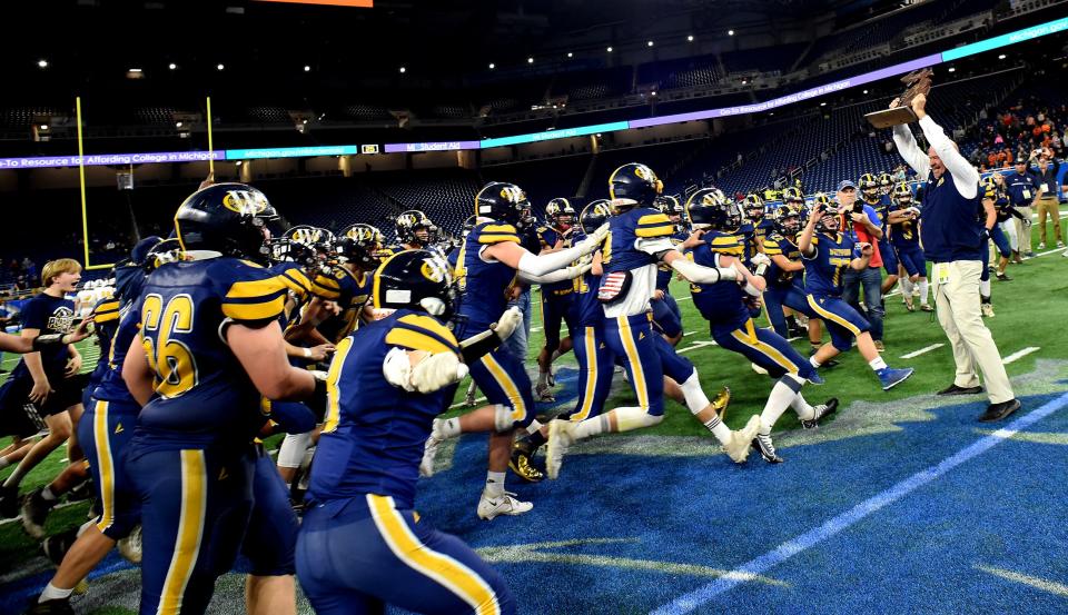 Whiteford coach Todd Thieken raises the state championship trophy as his players race towards him following a 26-20 win over Ubly in the Division 8 state finals at Ford Field Friday.