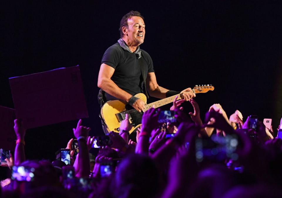 A man plays a guitar onstage with fans raising their arms in front of him