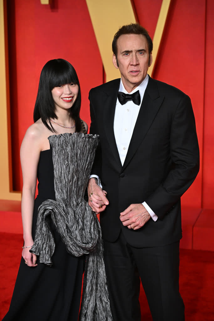 Two people pose together, one in a black tuxedo and the other in a strapless textured gown