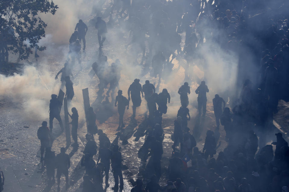 Protesters stand in tear gas launched by police amid ongoing demonstrations triggered by an increase in subway fares in Santiago, Chile, Monday, Oct. 21, 2019. (Photo: Esteban Felix/AP)