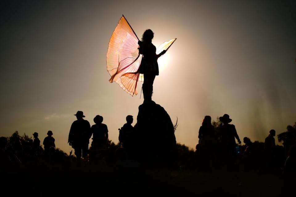 A festival attendee is silhouetted as they stand atop of the stone circle (PA)