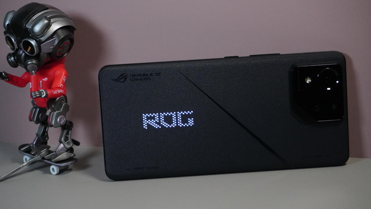  The Asus ROG Phone 8 on a grey and pink background, sat alongside some ROG merchandise. 