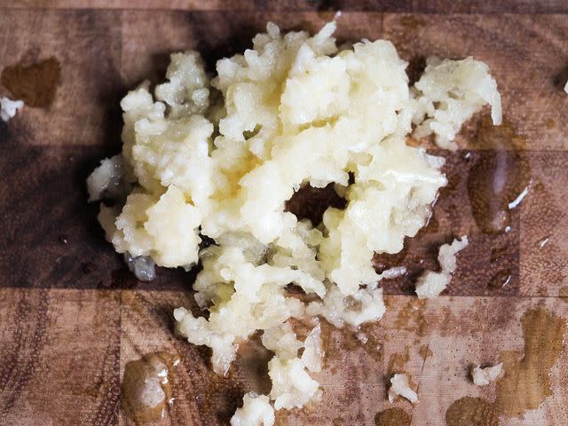 <p>Serious Eats / Daniel Gritzer</p> Garlic-pressed garlic, with some of the sprayed juices can be seen on the cutting board.