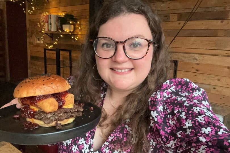 Woman with glasses holding a plate with a burger on