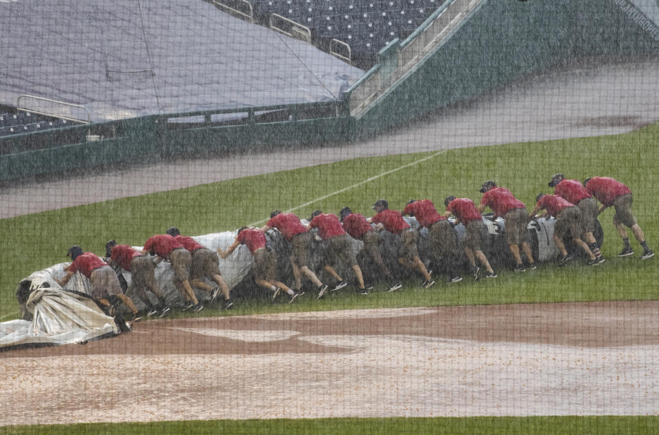 Grounds crew members unroll the tarp to cover the baseball diamond from a heavy downpour delaying the baseball game during the sixth inning of a baseball game between the Washington Nationals and the Baltimore Orioles in Washington, Sunday, Aug. 9, 2020. (AP Photo/Manuel Balce Ceneta)