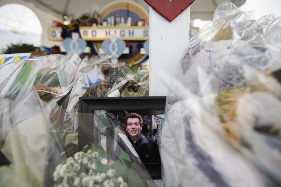 A photo of Oxford High School student Justin Schilling, who was one of the four students shot and killed during an active shooter at Oxford High School, sits amongst bouquets of flowers and other items left at a memorial at Oxford High School on Thursday, Dec. 9, 2021.