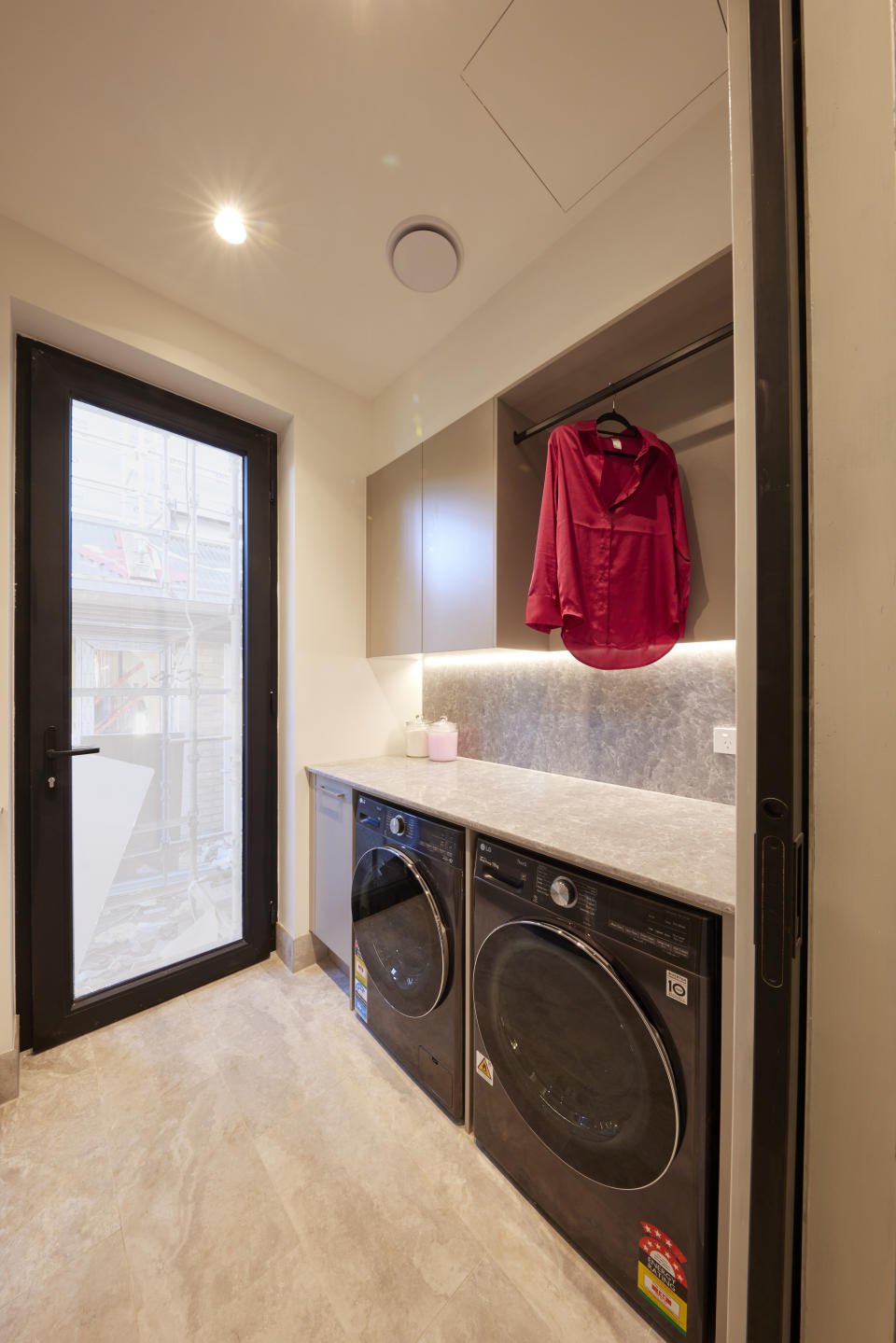 A photo of a washer and dryer with bench space above them and a hanging red button up shirt.