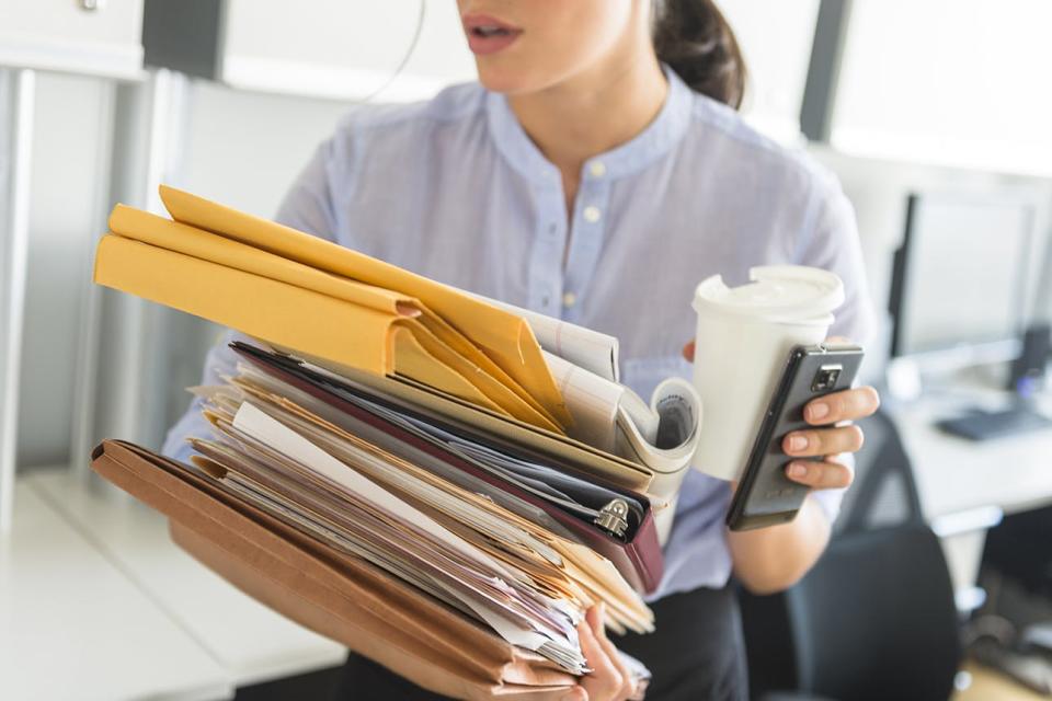 Woman carrying coffee, phone and stack of papers