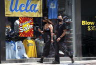 A couple wearing protective masks from the coronavirus walk down the street in the Westwood section of Los Angeles on Friday, May 15, 2020. Leaving home in Los Angeles now requires bringing a face covering, part of the price for reopening more businesses and activities in America's second-largest city, which is moving cautiously as less-populated areas of California press ahead. (AP Photo/Richard Vogel)