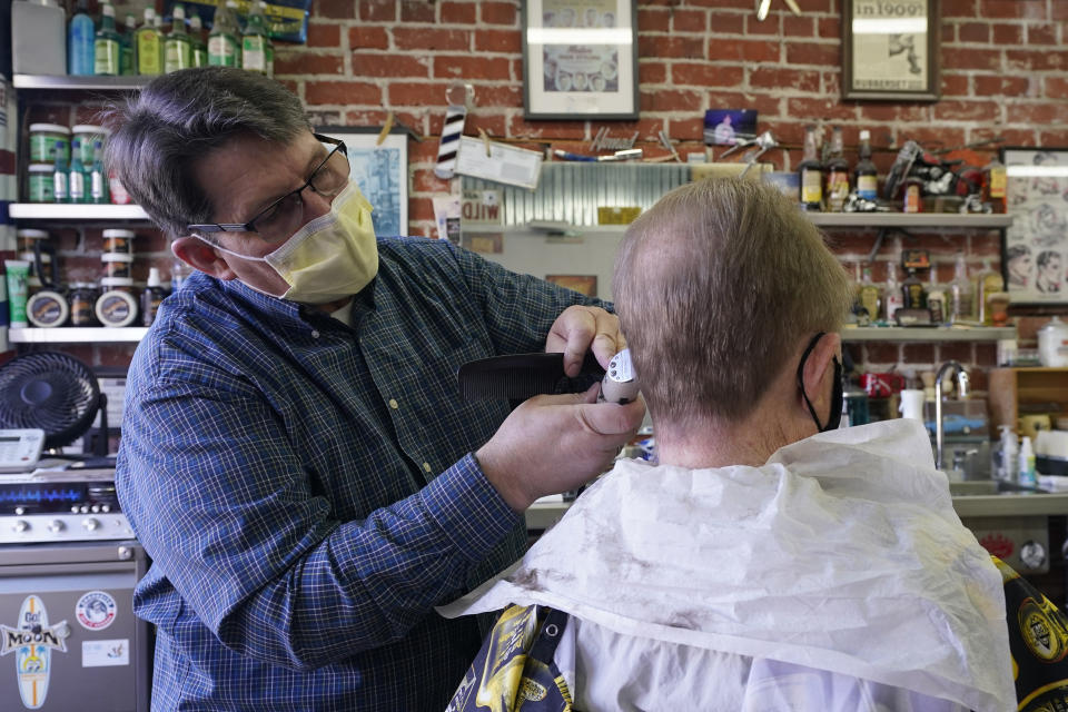 Mike Douglass, left, gives Kent Kjestrom a haircut at East J Barbers in Sacramento, Calif., Thursday, Jan. 21, 2021. Local officials and businesses in the 13-county Greater Sacramento region were caught off guard last week when outdoor dining and worship services were OK again, hair and nail salons and other businesses could reopen, and retailers could allow more shoppers inside. It's still a mystery how the state made the decision or how and when it will lift the most serious restrictions on the bulk of the state's population because officials won't share their data. (AP Photo/Rich Pedroncelli)