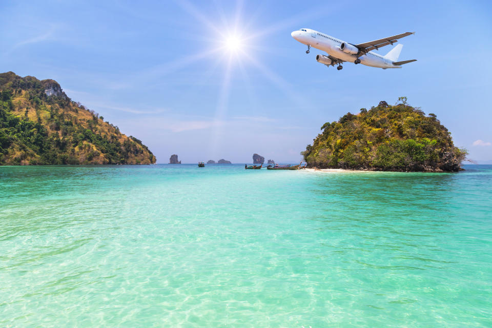 passenger airplane landing above small island in blue sea and tropical beach on blue sky with sunlight. travel destinations concept.
