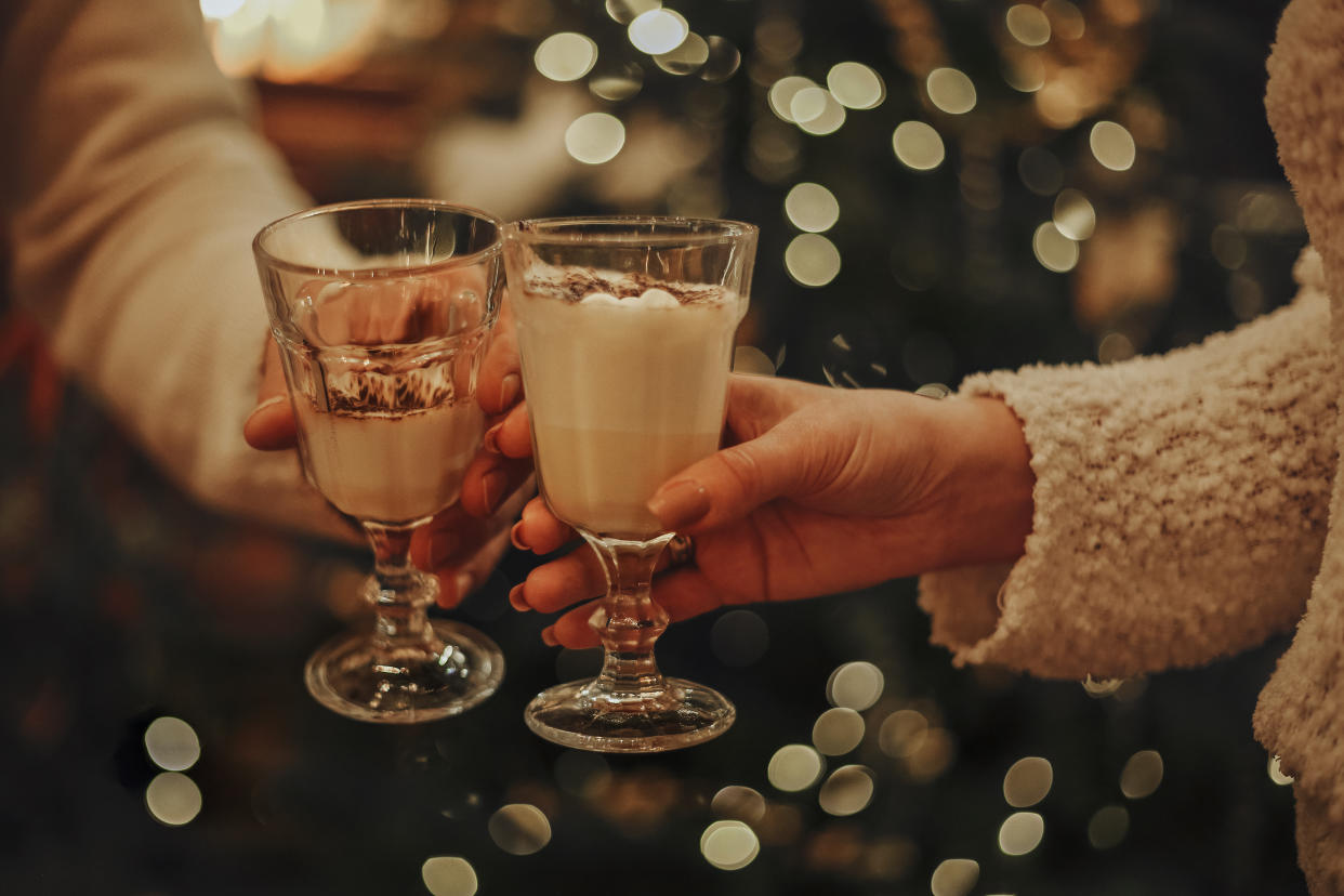 Two arms and hands clink glasses of eggnog in a holiday toast