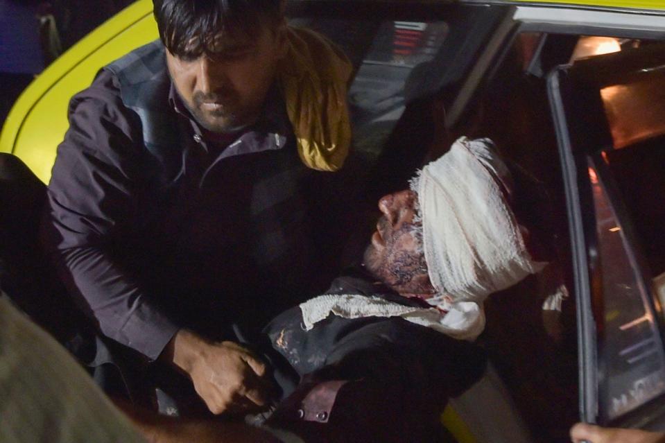 A hospital worker lifts an injured man, whose head is bandaged, out of a car for treatment