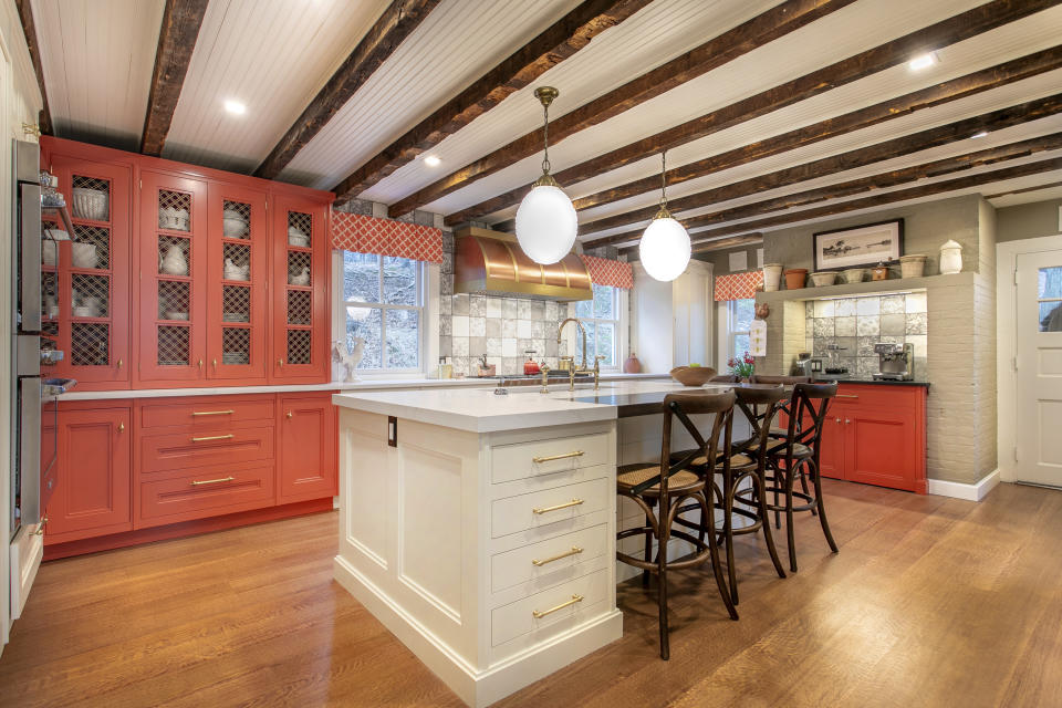 This image released by Bakes & Kropp shows the Cold Spring Harbor kitchen with hutch cabinetry and a coffee bar painted in Benjamin Moore’s fresh, cheerful Geranium, with white Farrow & Ball’s Lime White on the island and perimeter cabinets. Large lighting fixtures, like these from Hudson Lighting, add punctuation to the dramatic yet homey overall design. (Brandon C. Tobin /Bakes & Kropp via AP)