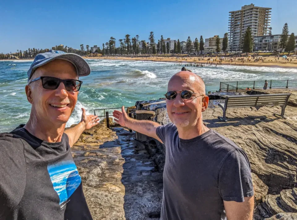 Brent and Michael standing on rocky headlands overlooking Manly Beach 