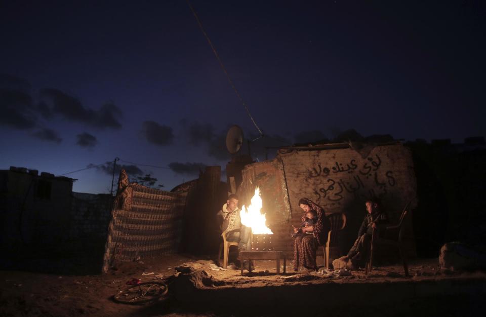In this Sunday, Jan. 15, 2017 photo, a Palestinian family warm themselves up with a fire outside their makeshift house during a power cut in a poor neighborhood in town of Khan Younis in the southern Gaza Strip. At night, large swaths of the Gaza Strip plunge into darkness _ the result of chronic and worsening power outages. In crowded city streets, the only source of light comes from the headlights of passing cars. The power shortages are the worst to hit Gaza since Hamas seized control of the territory 10 years ago. (AP Photo/ Khalil Hamra)