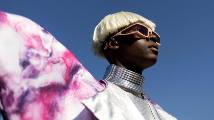 A model wears silver and batik clothing plus a blond wig.