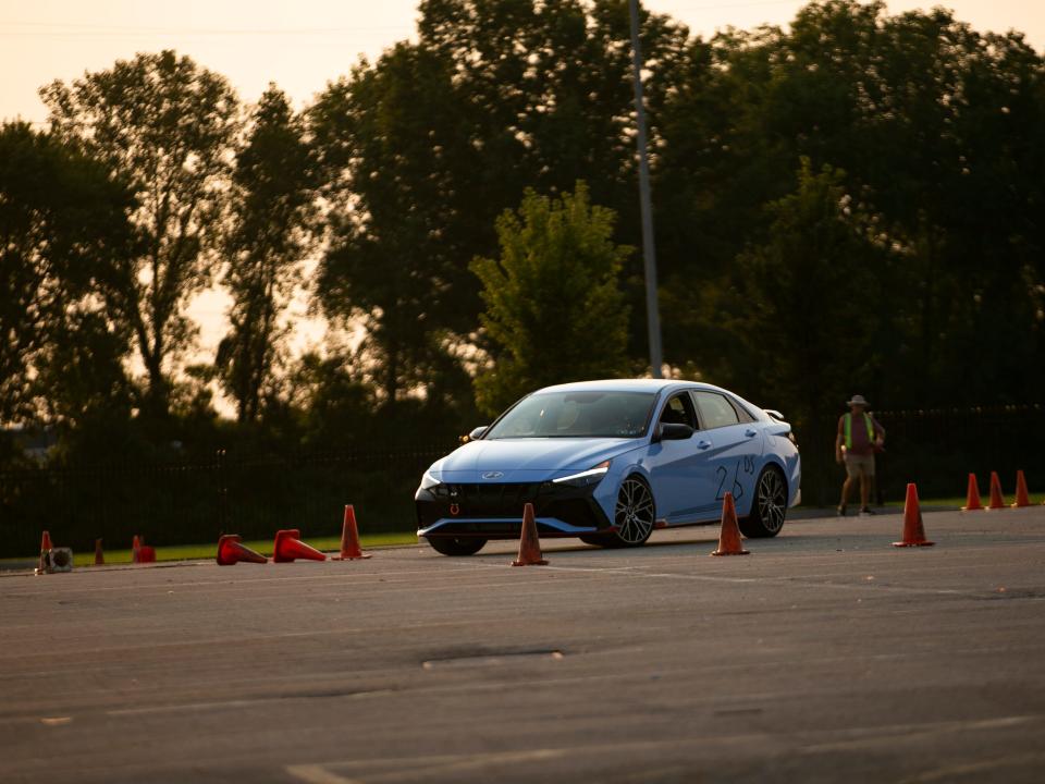 A blue Hyundai Elantra N on an autocross course turning around a set of traffic cones laying on their side, pointing in the direction of the car's turn.