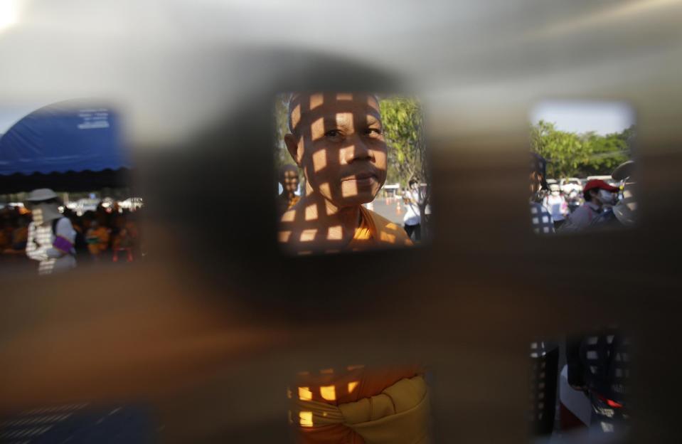 A Buddhist monk, his face in the shadow of the gate he is standing behind, waits inside Wat Dhammakaya temple in Pathum Thani province, Thailand, Thursday, Feb. 16, 2017. Hundreds of police in Thailand are carrying out a raid on the headquarters temple of a controversial Buddhist temple sect to detain its chief, a monk facing criminal charges including accepting $40 million in embezzled money. (AP Photo/Sakchai Lalit)