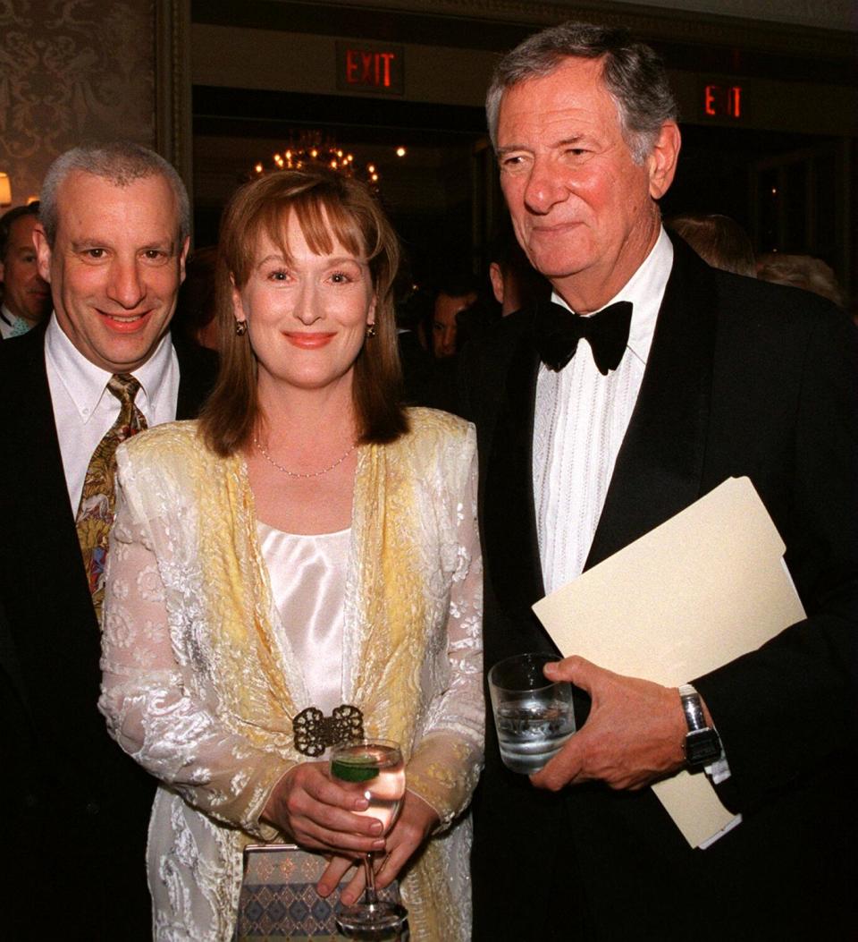 A man in a suit and a man in a tuxedo flank a woman