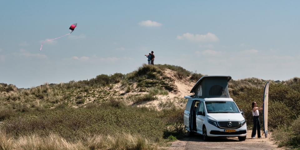 The van parked near people flying a kite.