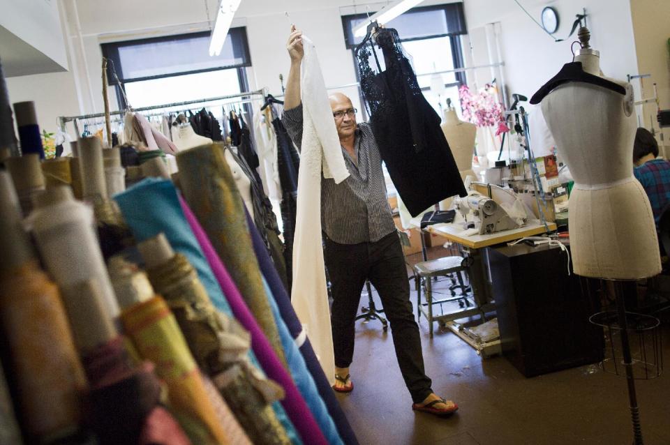 In this Aug 21, 2013 photo, fashion designer Carmen Marc Valvo carries dresses while putting together his Spring 2014 collection, in his studio in New York. Valvo says "the most rewarding part of building the collection is when you make your final edit and the run of show is set in stone and no more changes can be made." (AP Photo/John Minchillo)