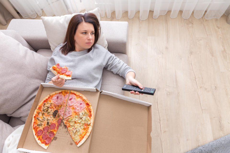 Frau liegt auf dem Sofa und isst Pizza