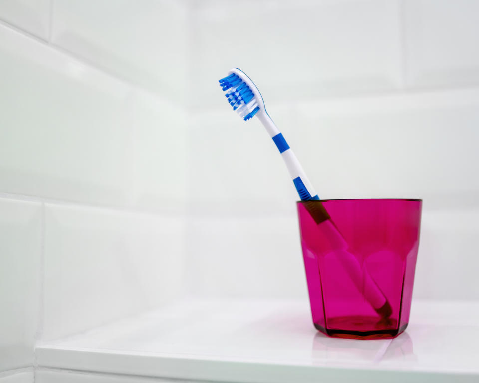 A still life of a single blue toothbrush standing alone in a pink toothbrush holder in a white tiled bathroom