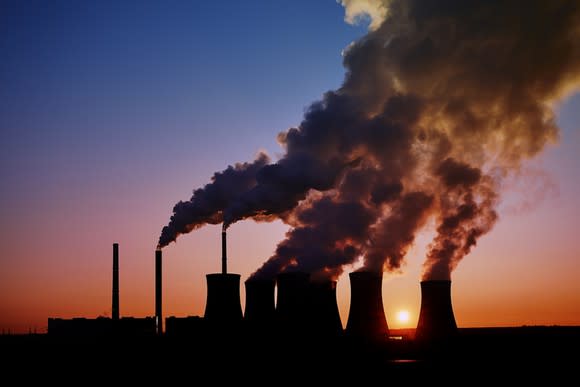 Steam rising from the cooling towers of a coal-fired power plant in silhouette.