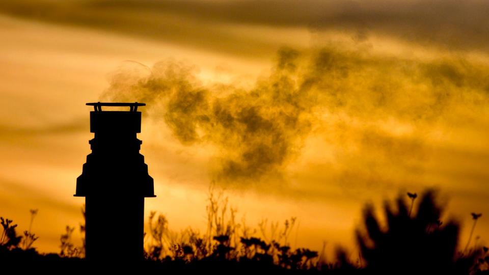 Ein kleiner Schornstein auf einem bepflanzten Dach entlässt bei Sonnenaufgang die Abgase einer Gasheizung in die eiskalte Morgenluft.