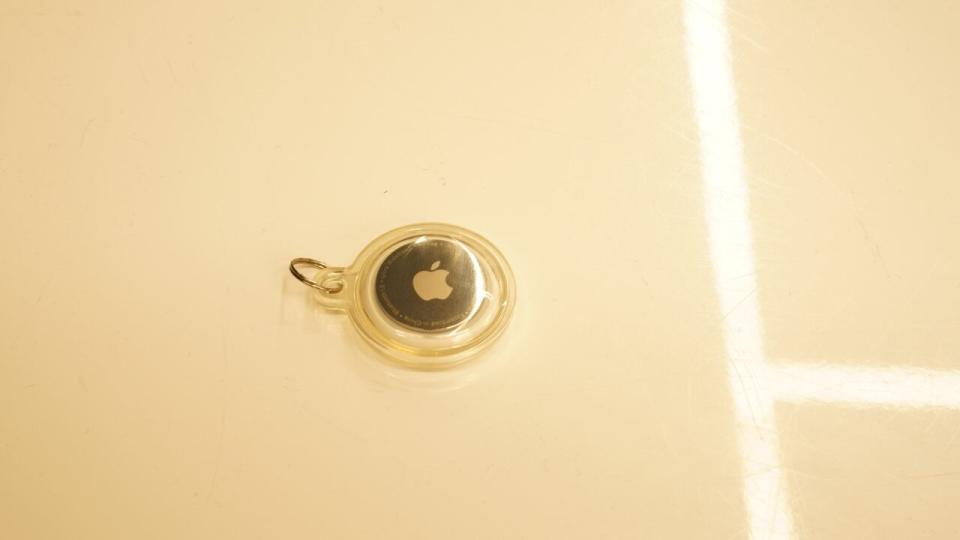 An apple airtag is seen on a white surface.