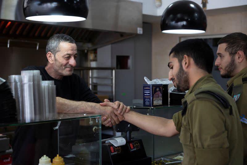 Zroya, the owner of Shawarma restaurant holds the hand of an Israeli soldier in Ramla