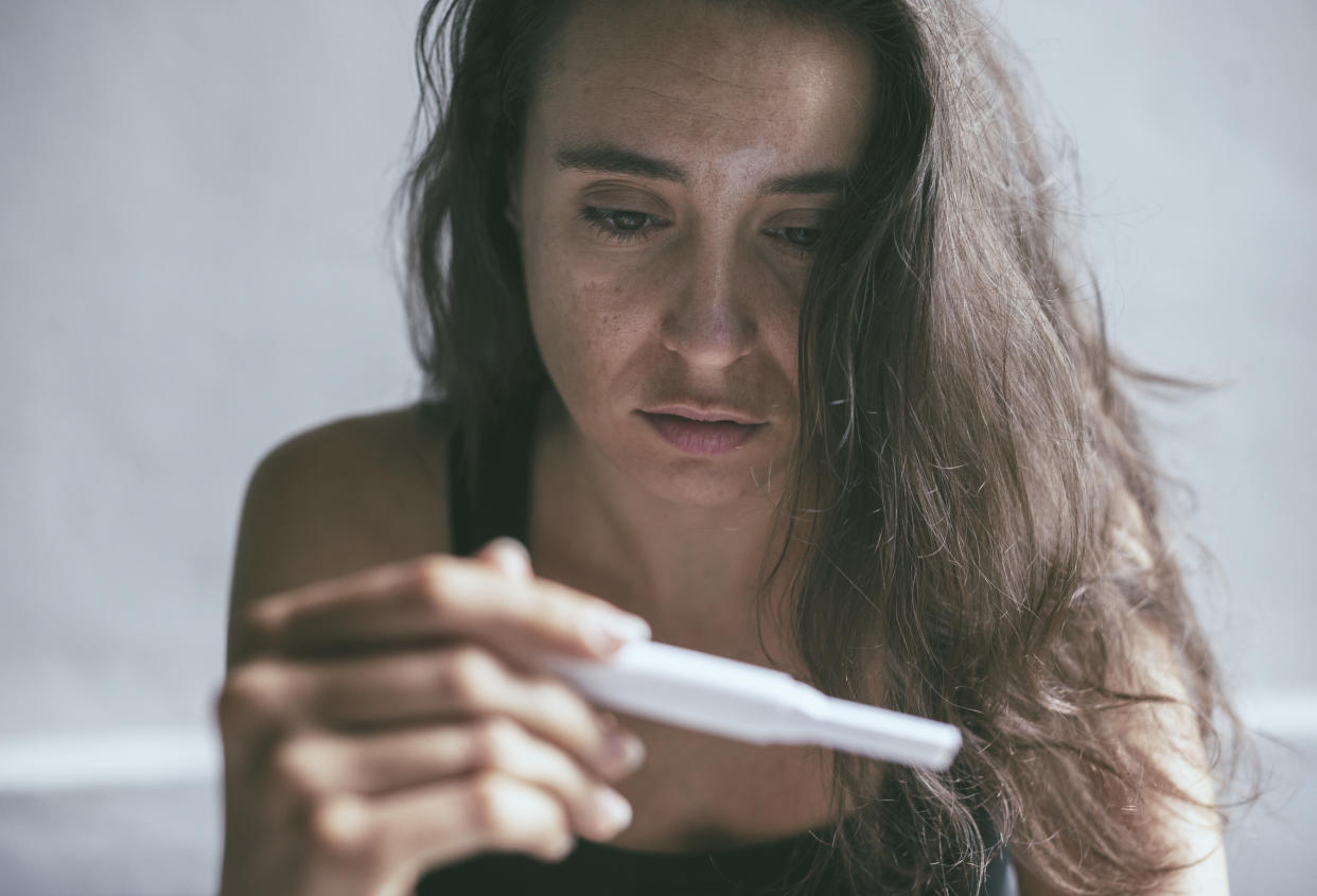 A woman somberly looks at a pregnancy test tool she’s holding in her hand.