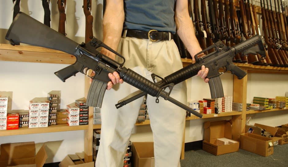 A man holds two assault rifles across his thighs in a sporting-goods store.