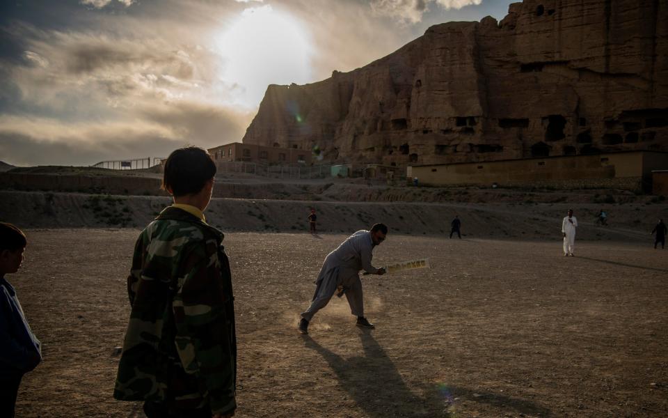Children play cricket in front of the big Buddha in Bamiyan city